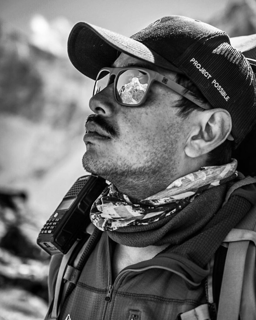 picture of Nirmal Purja in black and white with a reflection of the mountains over his sunglasses